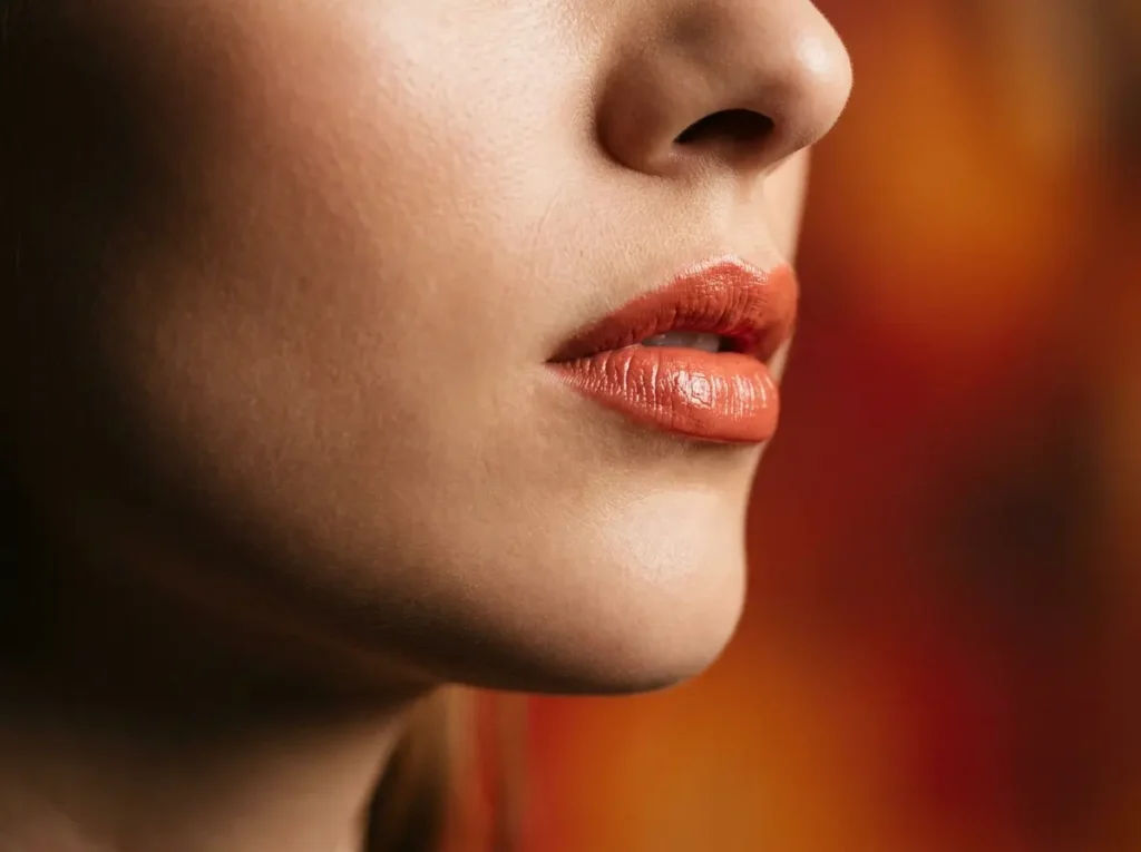Boca em 3/4 com batom coral-terracota, close editorial