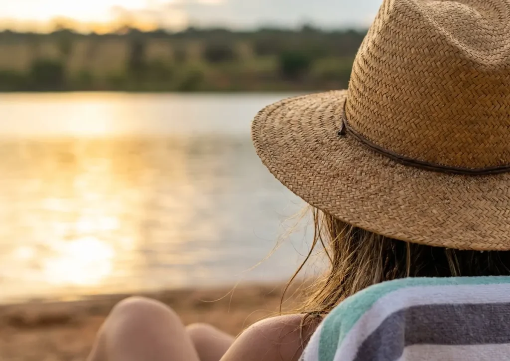 Praias perto de Brasília para um fim de semana: rotas e custos Mulher de costas com chapéu de palha na beira de praia fluvial ao pôr do sol