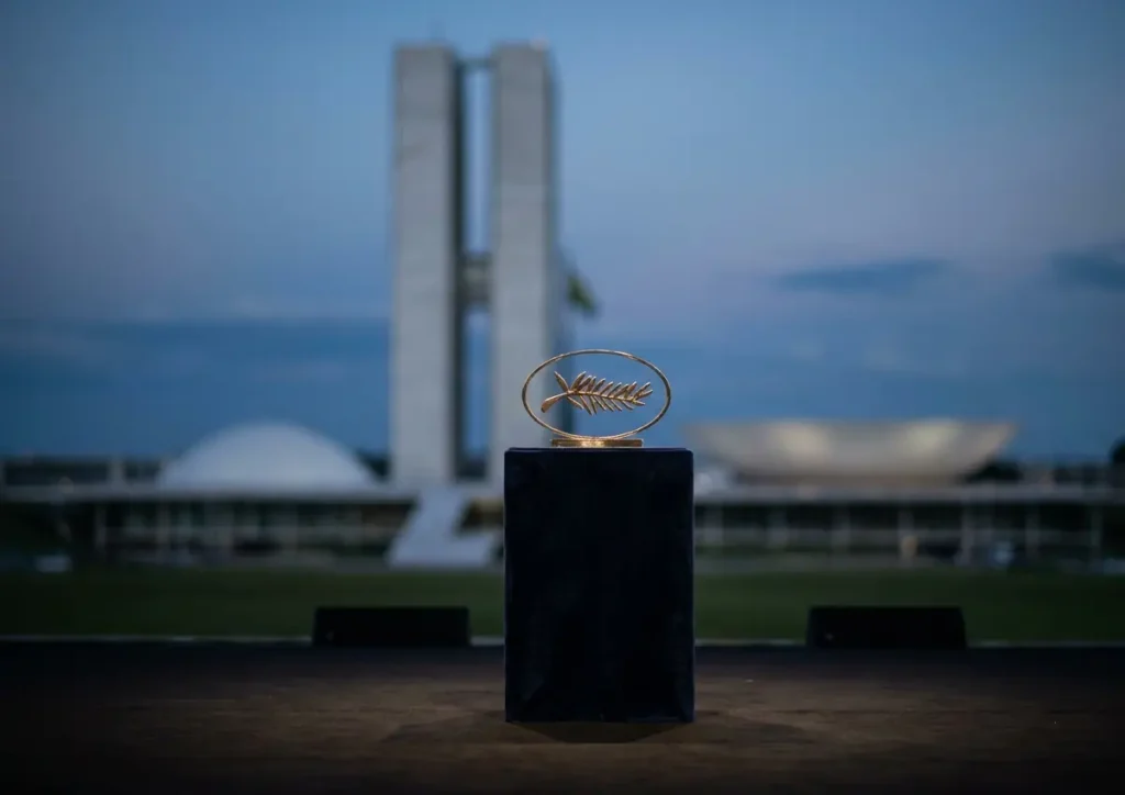 Troféu da Palma de Ouro em pedestal com o Congresso Nacional desfocado ao fundo
