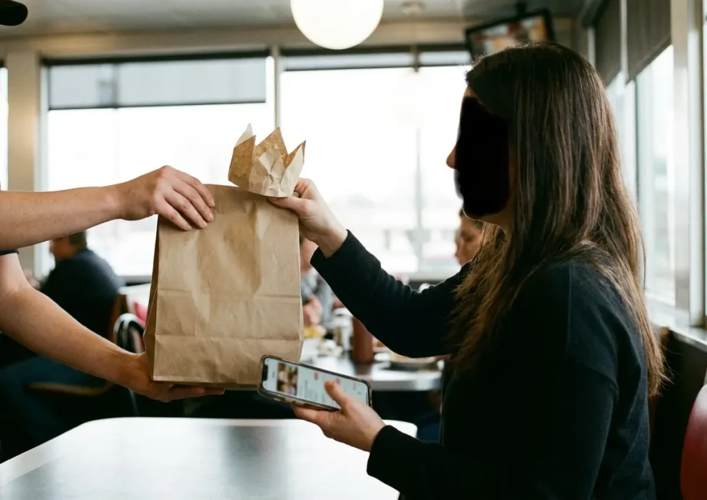 Burger King lança ofertas no app para dia das mães e movimenta Brasília Mãe de perfil recebe sacola para viagem enquanto segura celular com ofertas desfocadas.