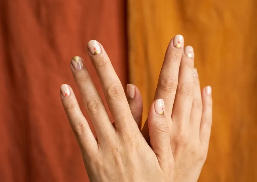 Mãos femininas com unhas curtas decoradas em tons quentes e detalhes dourados, composição editorial de alto impacto