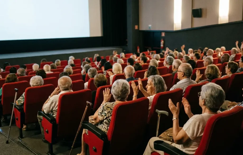 Sala do Cine Brasília com poltronas vermelhas cheias de idosos vistos de costas e em perfil, luz da tela iluminando silhuetas