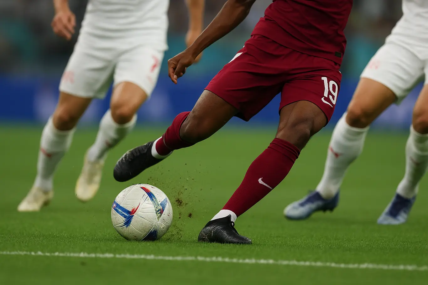 Close do pé do atacante do Catar chutando a bola nos acréscimos, grama levantada
